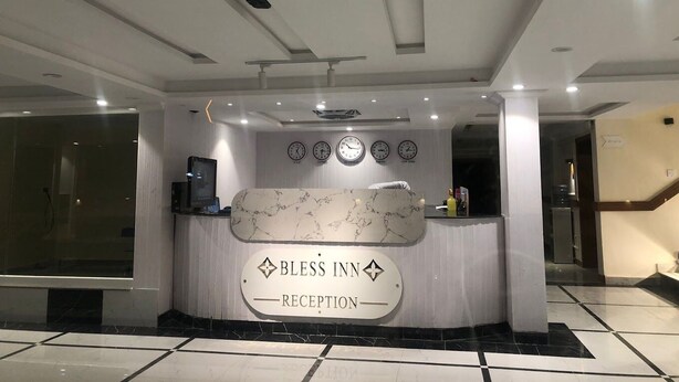 Una zona de recepción con un mostrador de mármol, relojes y un cartel que dice 'Bless Inn Reception'.