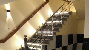 Una escalera con barandilla de madera y pasamanos metálico, que conduce a un rellano con una lámpara.
