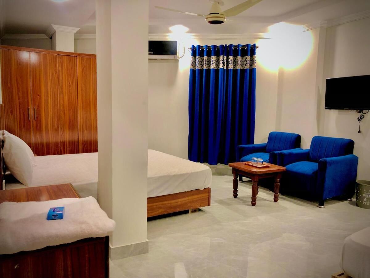 Een hotelkamer met een bed, een bank, een salontafel en twee blauwe fauteuils.