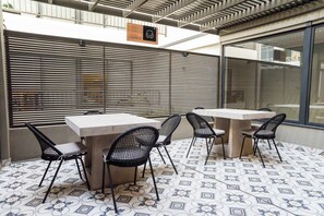 A terrace with tables and chairs, a sign for 'Teagraza Lounge', and patterned floor tiles.