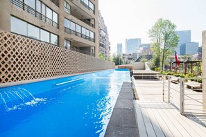A swimming pool with a wooden deck, a lattice fence, and a cityscape in the background.