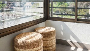 A room with large windows, two woven ottomans, and a view of buildings.