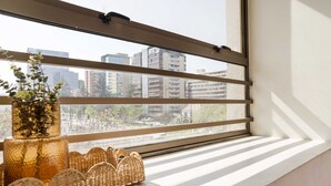 A window with horizontal blinds, a wicker basket, and a vase with flowers.