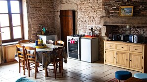 A rustic kitchen with a stone wall, wooden cabinets, a dining table with chairs, and a small oven. - Large apartment with raised garden in the heart of Burgundy (Montcenis)