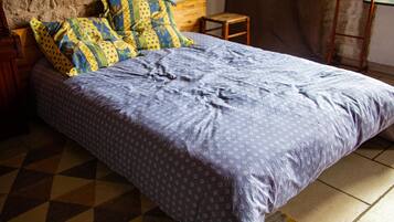 Un letto con copriletto blu e viola decorato, una testiera in legno e un tappeto anch'esso decorato su un pavimento a scacchi.