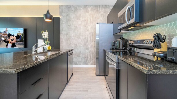Une cuisine moderne dotée de plans de travail en granit, d’appareils électroménagers en acier inoxydable et d’un grand îlot central.