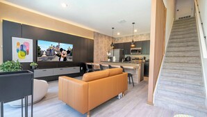 Un salon moderne avec un canapé, un téléviseur à écran plat et un escalier menant à un espace cuisine.