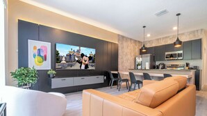 Un salon moderne comprenant un canapé, un téléviseur et un coin cuisine équipé d’un four à micro-ondes et de placards.