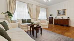 A spacious living room with a large sofa, two armchairs, a wooden coffee table, and a chandelier.