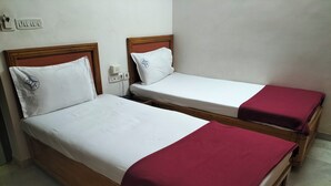 Dos camas individuales con estructura de madera y ropa blanca, una con una manta roja.