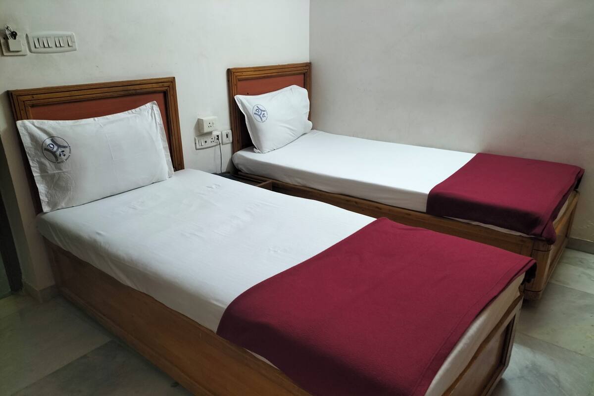 Two single beds with wooden frames and white bedding, one with a red blanket.