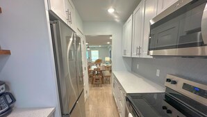Una cocina moderna con electrodomésticos de acero inoxidable, piso de madera y armarios blancos.