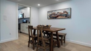 A dining area with a wooden table and chairs, a painting on the wall, and a kitchen in the background. - 🌊 Welcome to Little Bay Landing in Rockport, Texas! 🌊 (Rockport)