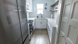 Cocina compacta con armarios blancos, un refrigerador de acero inoxidable y una ventana que proporciona luz natural.