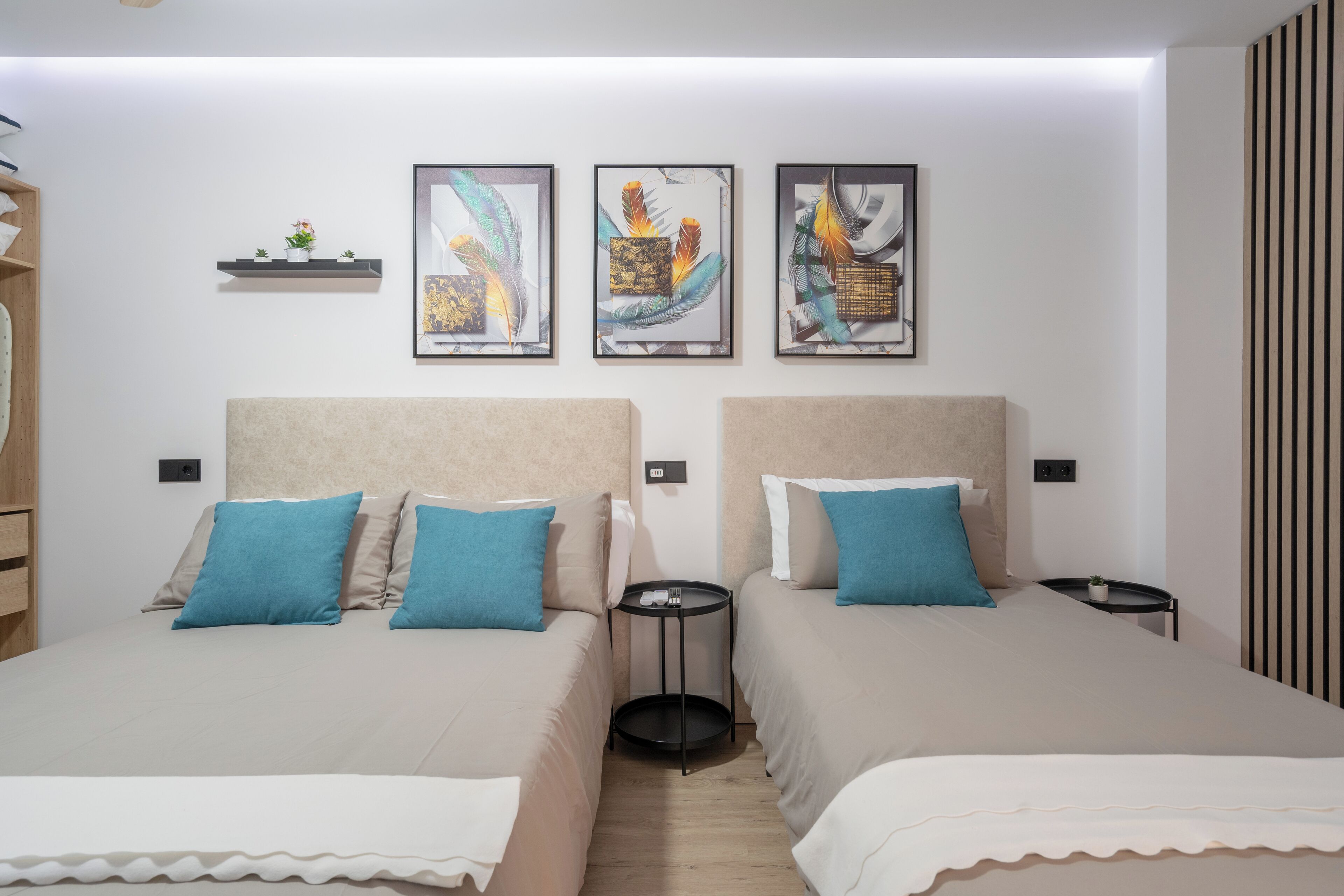 Une chambre d’hôtel moderne avec deux lits, une petite table ronde et trois œuvres d’art encadrées accrochées au mur.