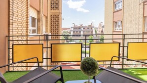 A balcony with two lounge chairs, a small potted plant, and a view of surrounding buildings.