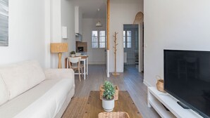 Una sala de estar moderna con un sofá, una mesa de centro con una planta, un televisor sobre un mueble bajo y un escritorio con una lámpara.