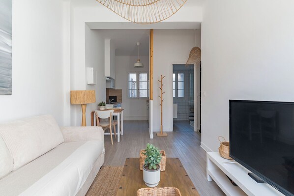 A modern living room with a sofa, a coffee table with a plant, a TV on a stand, and a desk with a lamp.