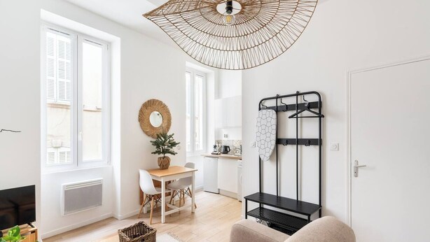 A modern living room with a dining area, a kitchen in the background, and a black metal rack with hangers.