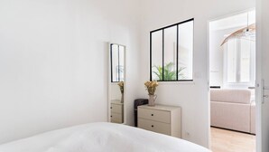 A minimalist bedroom with a large bed, a dresser, a mirror, and a window with a view of the outdoors.