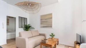 A modern living room with a beige sofa, a wooden coffee table, a wicker hanging light fixture, and a flat-screen TV on a wooden stand.