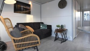 Una sala de estar moderna con un sofá negro, una silla de mimbre, una pequeña mesita de madera y una lámpara de pie.