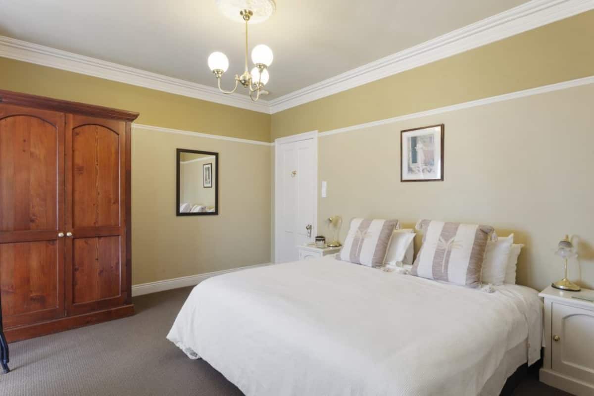 Une chambre à coucher avec un grand lit, une armoire en bois, une porte blanche et un lustre.