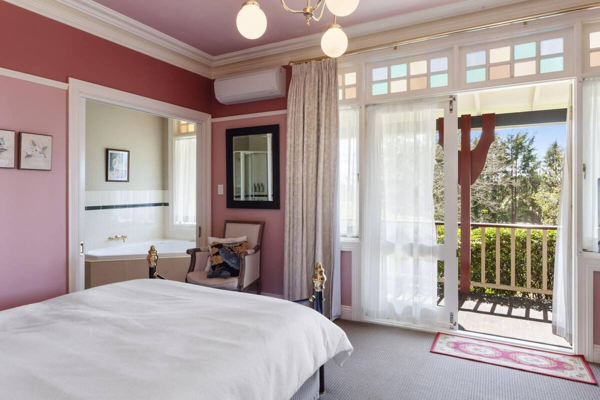 Une chambre à coucher comprenant un lit, une coiffeuse, une chaise, une fenêtre avec des rideaux et un balcon avec une balustrade.