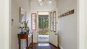 Un pasillo con un banco de madera, un jarrón con flores, una lámpara de pared y una puerta con paneles de vidrio artístico.