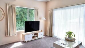 A modern living room with a flat-screen TV, a white console table, and a large window with curtains.