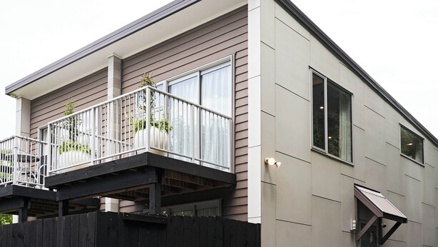 A modern two-story house with a balcony, large windows, and a small awning.