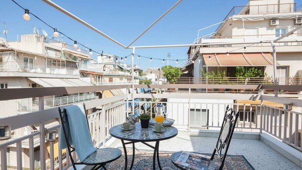 A balcony with a table, chairs, and a potted plant. - Neos Kosmos Gem with Balcony and Acropolis View (Athina)