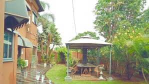 A courtyard with a covered seating area, a tiled pathway, and surrounding greenery. - La Belva Court with Swimming Pool (Lusaka)