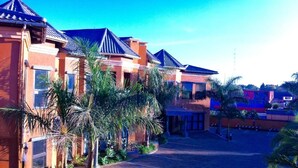 A hotel with multiple buildings, palm trees, and a paved driveway. - La Belva Court with Swimming Pool (Lusaka)