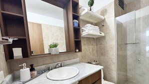 A modern bathroom with a marble sink, a large mirror, and a glass-enclosed shower.