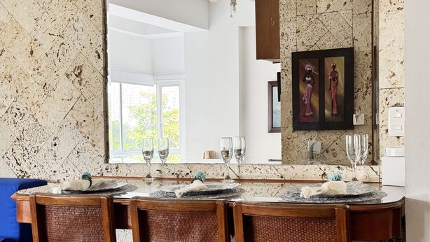 A dining area with a marble-tiled wall, a large mirror, and a framed artwork above the mirror.