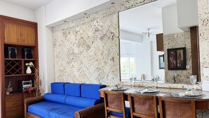 A modern living room with a blue sofa, wooden cabinet, and dining area with a large mirror and table set for dining.