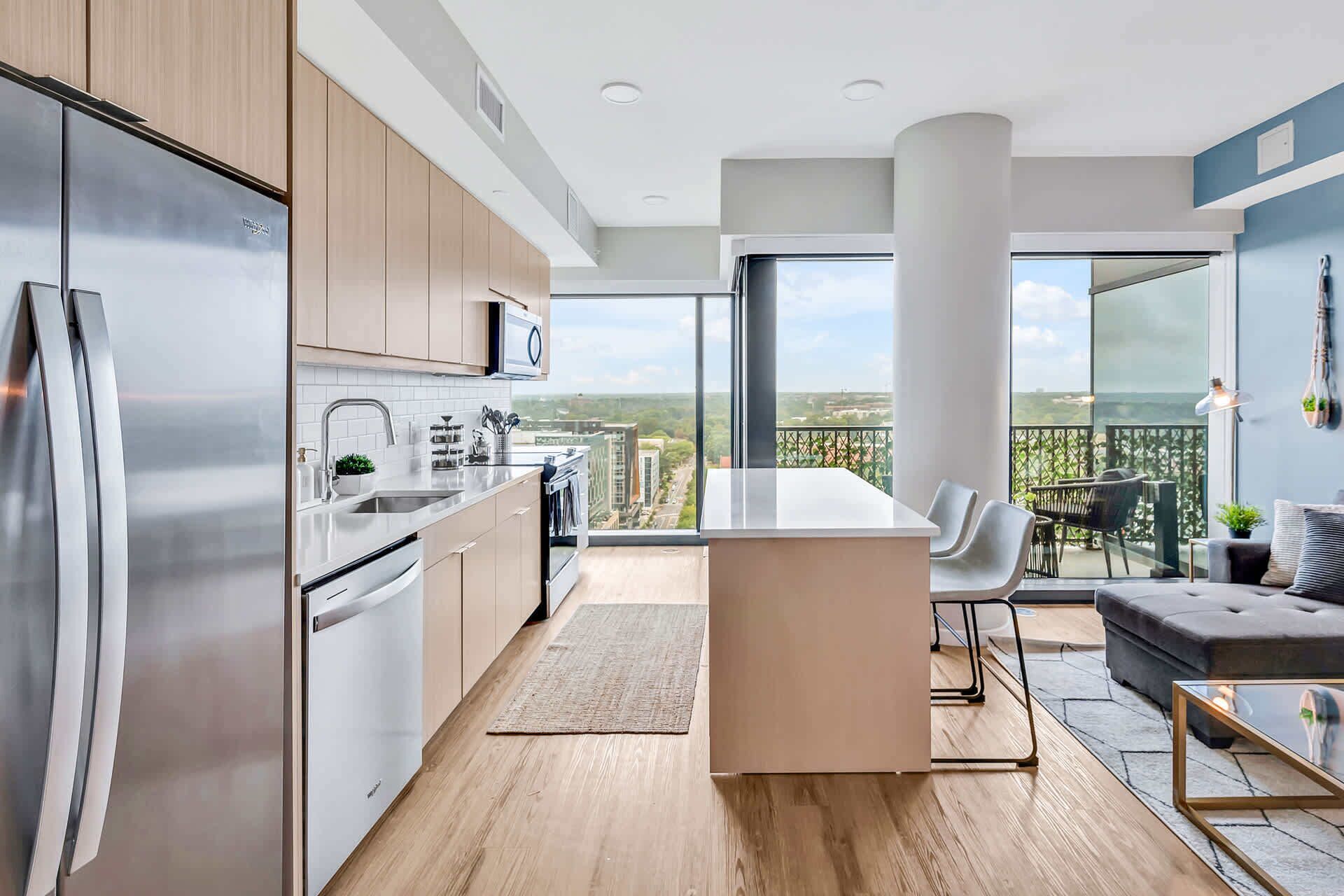 Cozinha moderna com eletrodomésticos de aço inoxidável, uma ilha central e vista para o horizonte urbano através de amplas janelas.