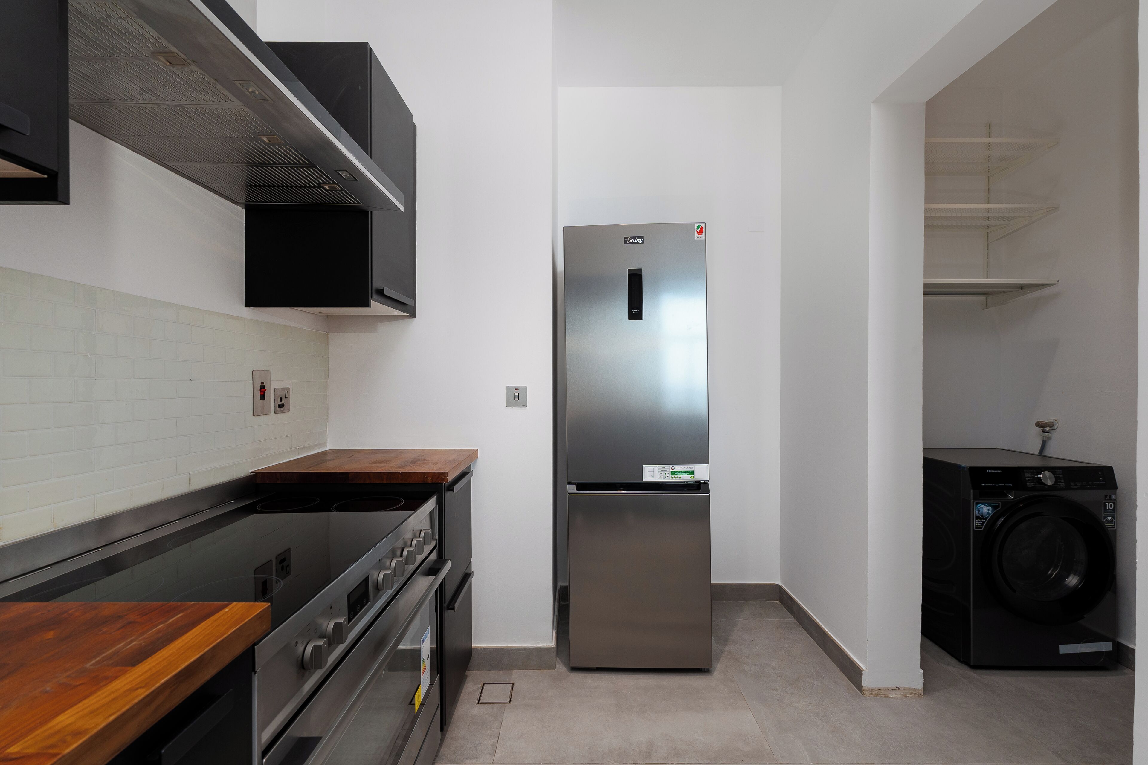 A compact kitchen with a stainless steel refrigerator, a built-in oven, and a washing machine.