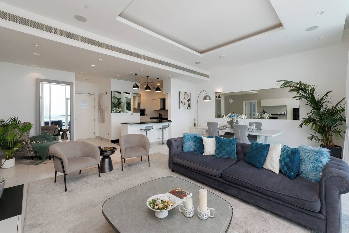 A modern living room with a grey sofa, a coffee table, and a dining area in the background.