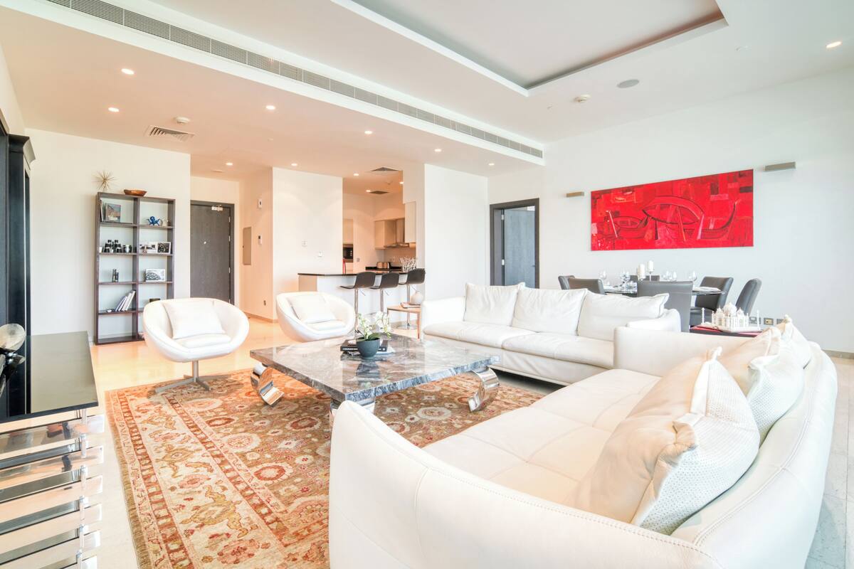 A modern living room with a white sofa, a coffee table, and a red abstract painting on the wall.