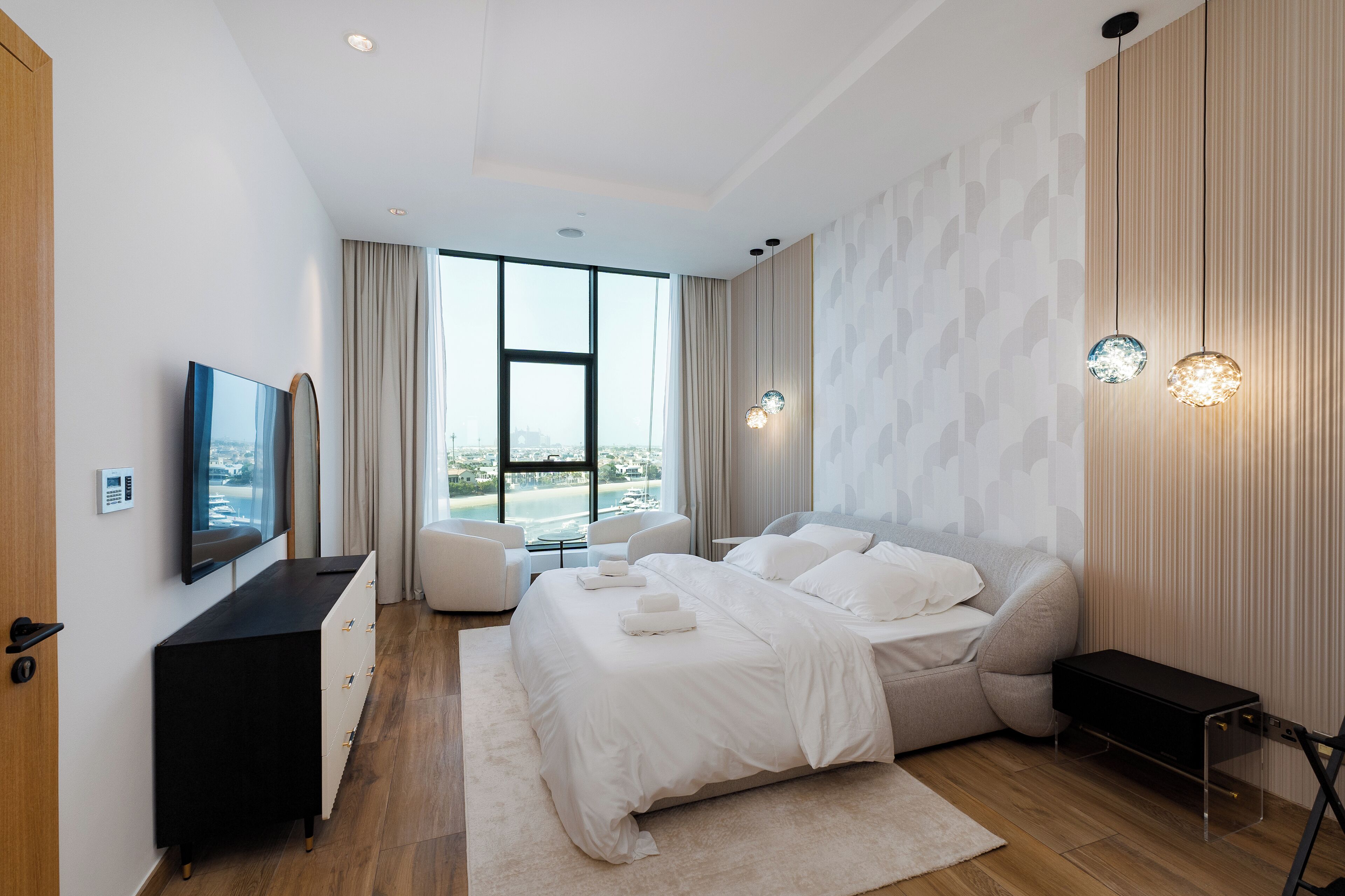 A modern bedroom with a large bed, a TV, a desk, and a view of the outdoors.