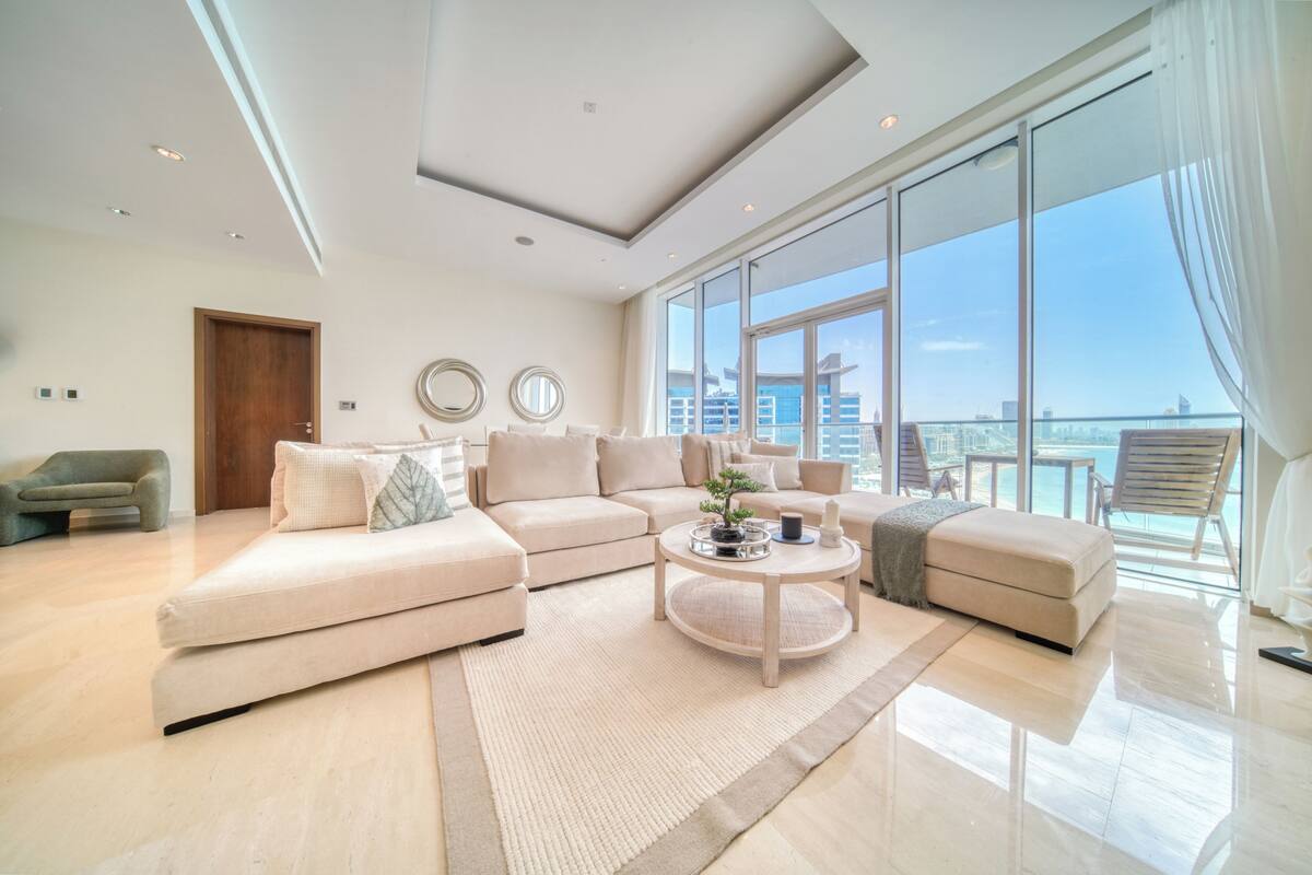 A spacious living room with a large sectional sofa, a round coffee table, and a view of the city through large windows.