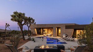 Un espace piscine extérieur moderne, doté de chaises longues, d’un foyer et aménagé dans un décor évoquant le désert.