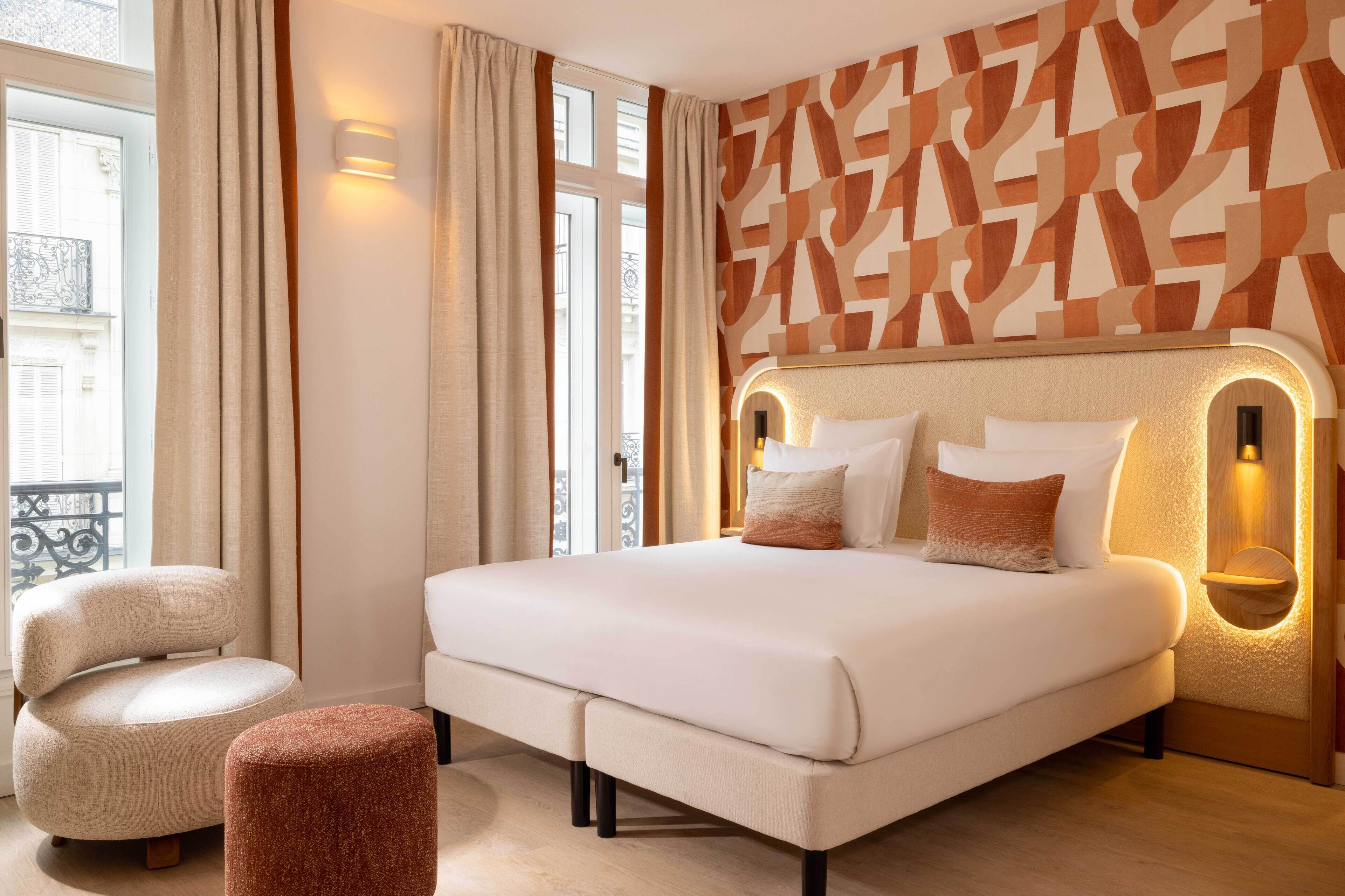 A modern hotel room with a large bed, a chair, and a small ottoman.