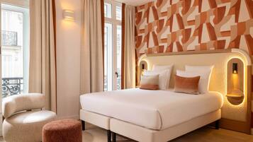 A modern hotel room with a large bed, a chair, and a small ottoman.