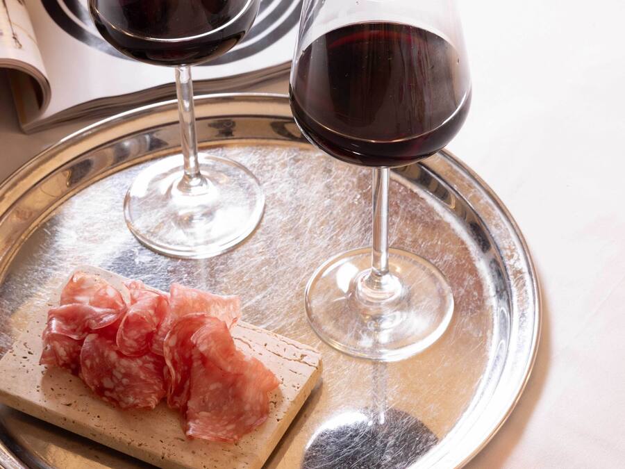 Una bandeja con dos copas de vino tinto y una loncha de embutido sobre una mesa.