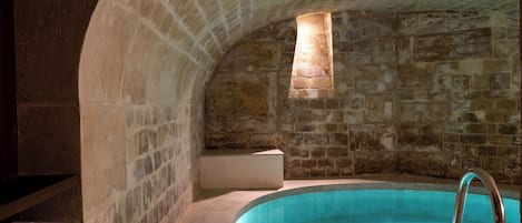 A stone-walled room with a built-in swimming pool and a small window.