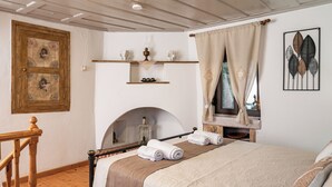 A bedroom with a bed, a wooden staircase, a fireplace, and a window with curtains. - THALIA'S COTTAGE - Cozy, Romantic Retreat for Two (Samos)
