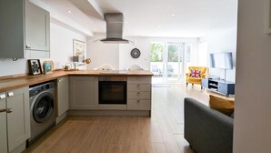 A modern kitchen with a built-in oven, a washing machine, and a dining area with a sofa and a TV. - Newquay Escape/10 min to Beach/patio/parking (Newquay)
